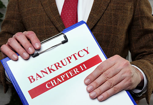 Attorney holding Chapter 11 bankruptcy clipboard; corporate debt restructuring help. - Wayne Greenwald, P.C.